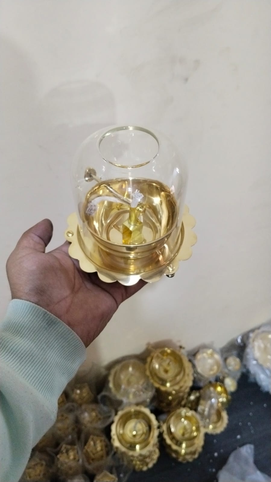 Hand holding a small glass container with a gold base on a light background
