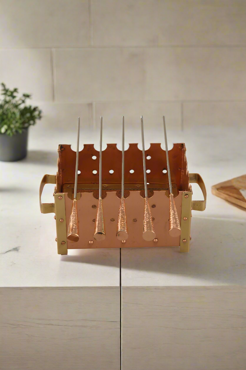 A bronze-colored barbeque grill with multiple grilling areas, situated on a patio with a white wall and greenery in the background. - Eco-friendly - Sama Homes