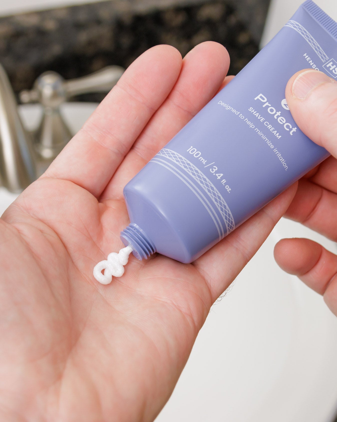 Hand holding a purple bottle of sunscreen cream with a small amount on the palm. - Image 5